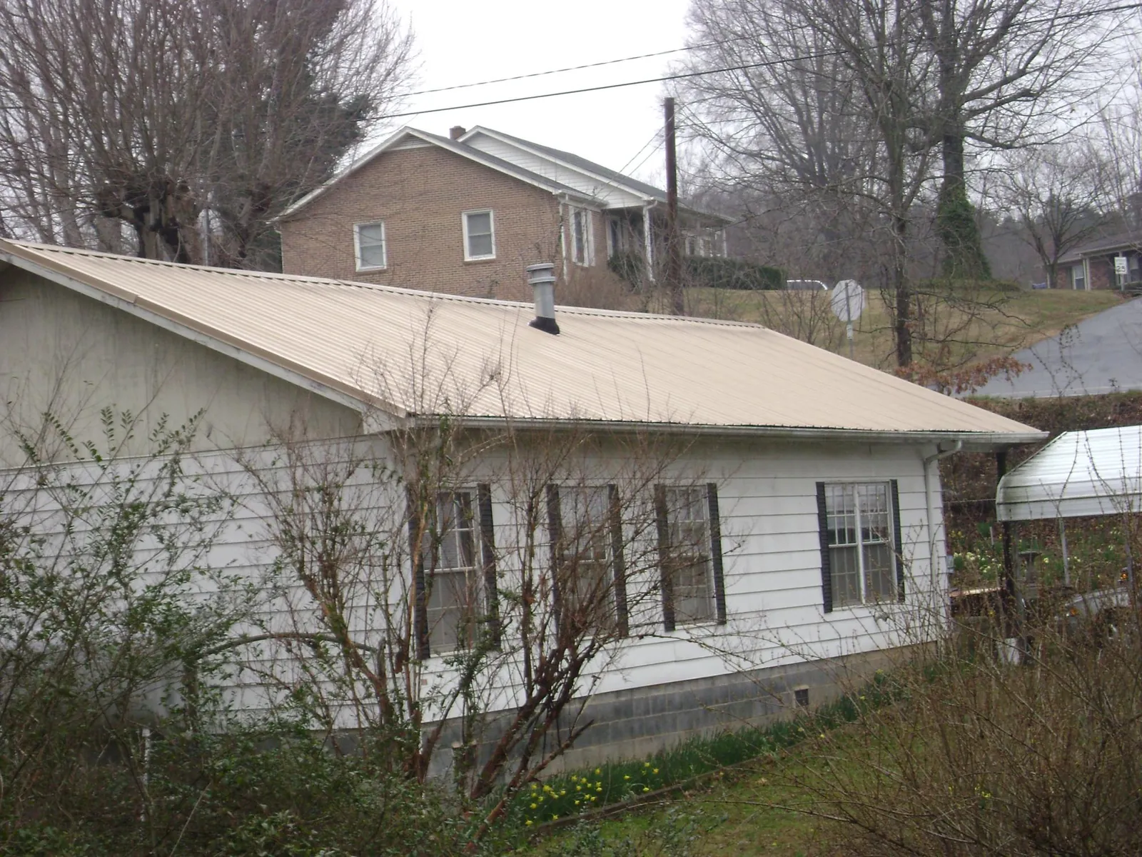 Tan metal roof on a white sided house set into a hillside — Commercial Roofing by Roofing Brothers in Bellevue